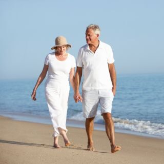 Smiling senior couple dressed in white walking along a sandy beach, representing Belle Vie Travel clients.